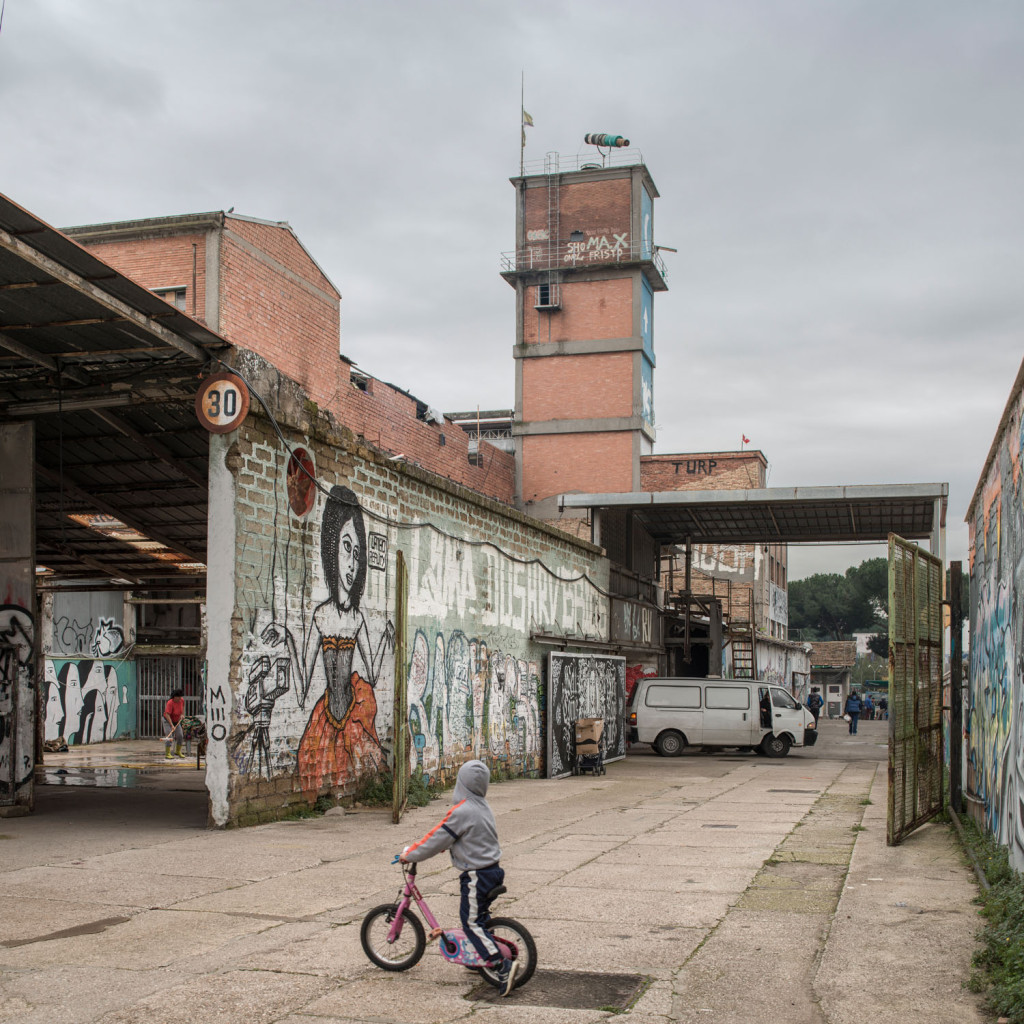 MAAM – Cortile esterno. Un bambino sulla sua bici. Sullo sfondo la torre di Metropoliz con in cima il telescopio di Gian Maria Tosatti – photo Giuliano Ottaviani