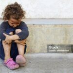 poor, sad little child girl sitting against the concrete wall